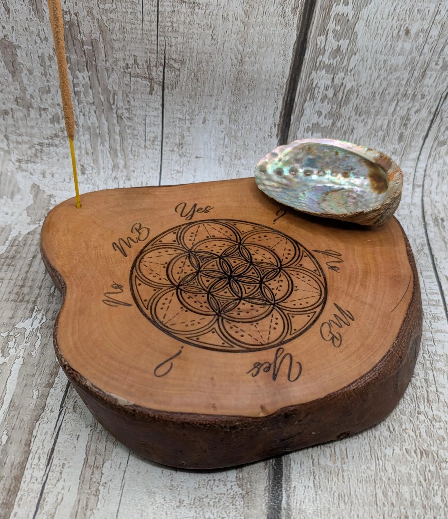 Wooden tree slice dowsing board with geometric laser print design, incense stick holder and loose abalone shell for crystals and herbs.