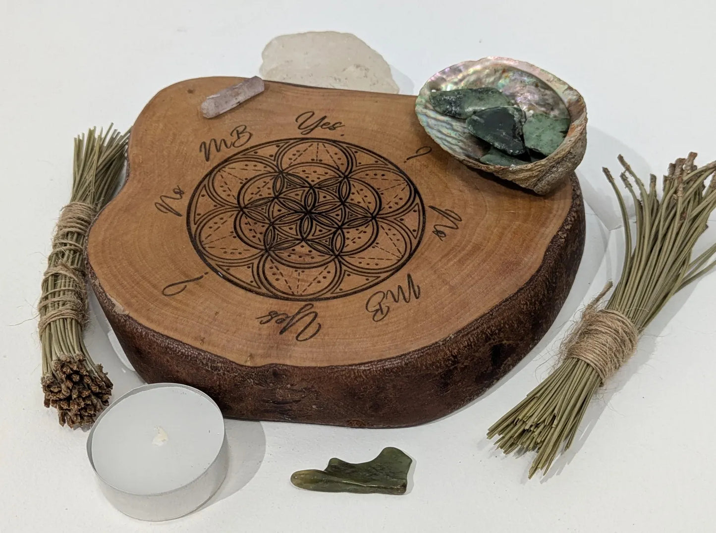 Wooden tree slice dowsing board with geometric laser print design, incense stick holder and loose abalone shell for crystals and herbs.
