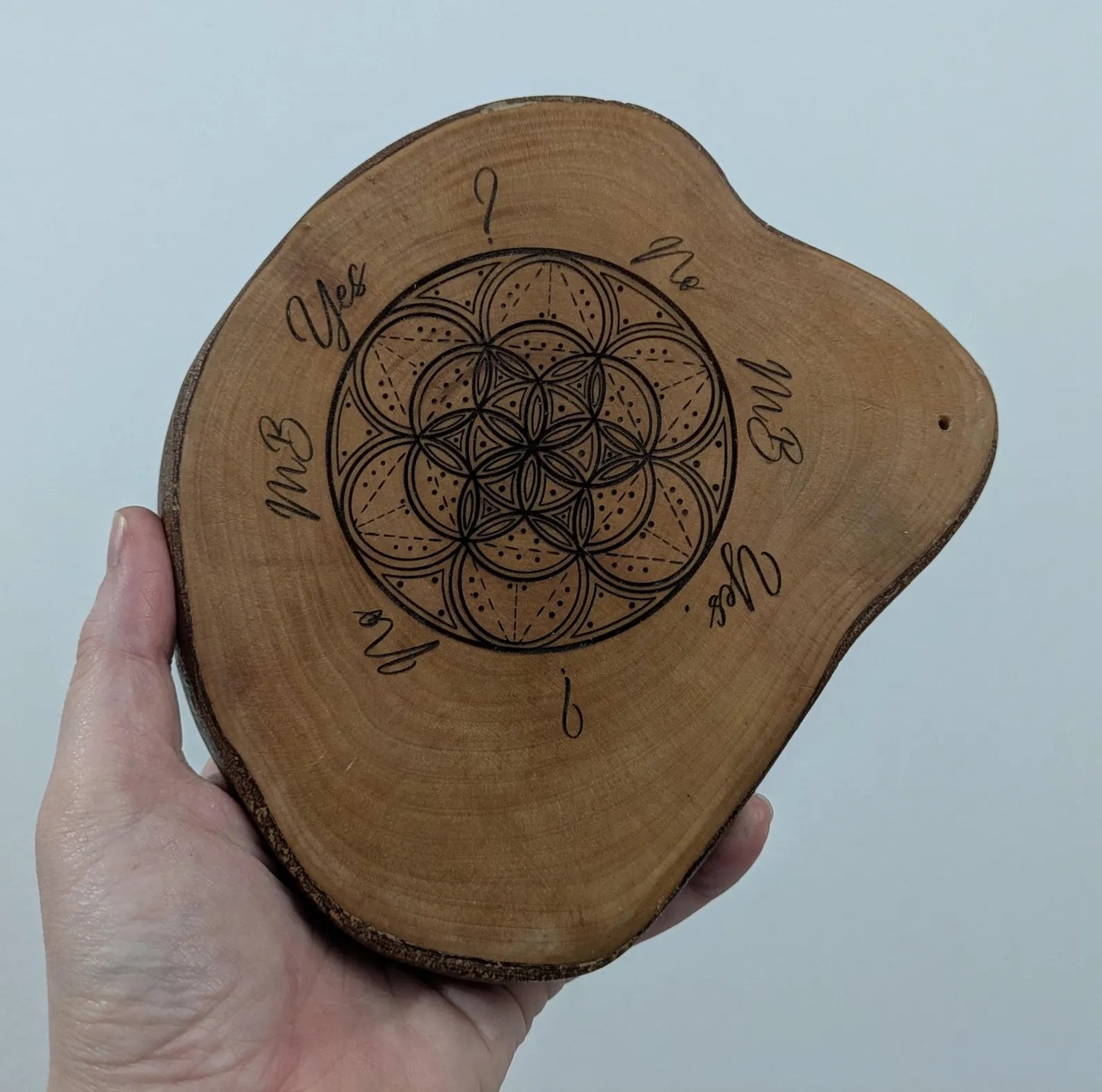 Wooden tree slice dowsing board with geometric laser print design, incense stick holder and loose abalone shell for crystals and herbs.