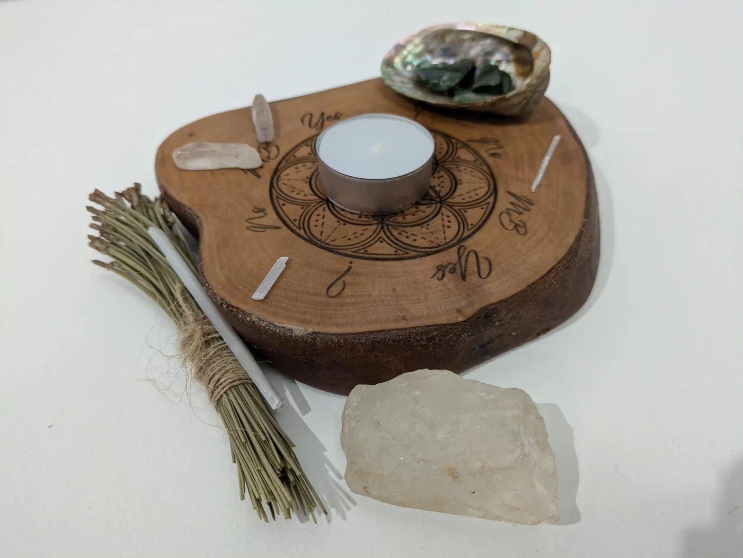 Wooden tree slice dowsing board with geometric laser print design, incense stick holder and loose abalone shell for crystals and herbs.