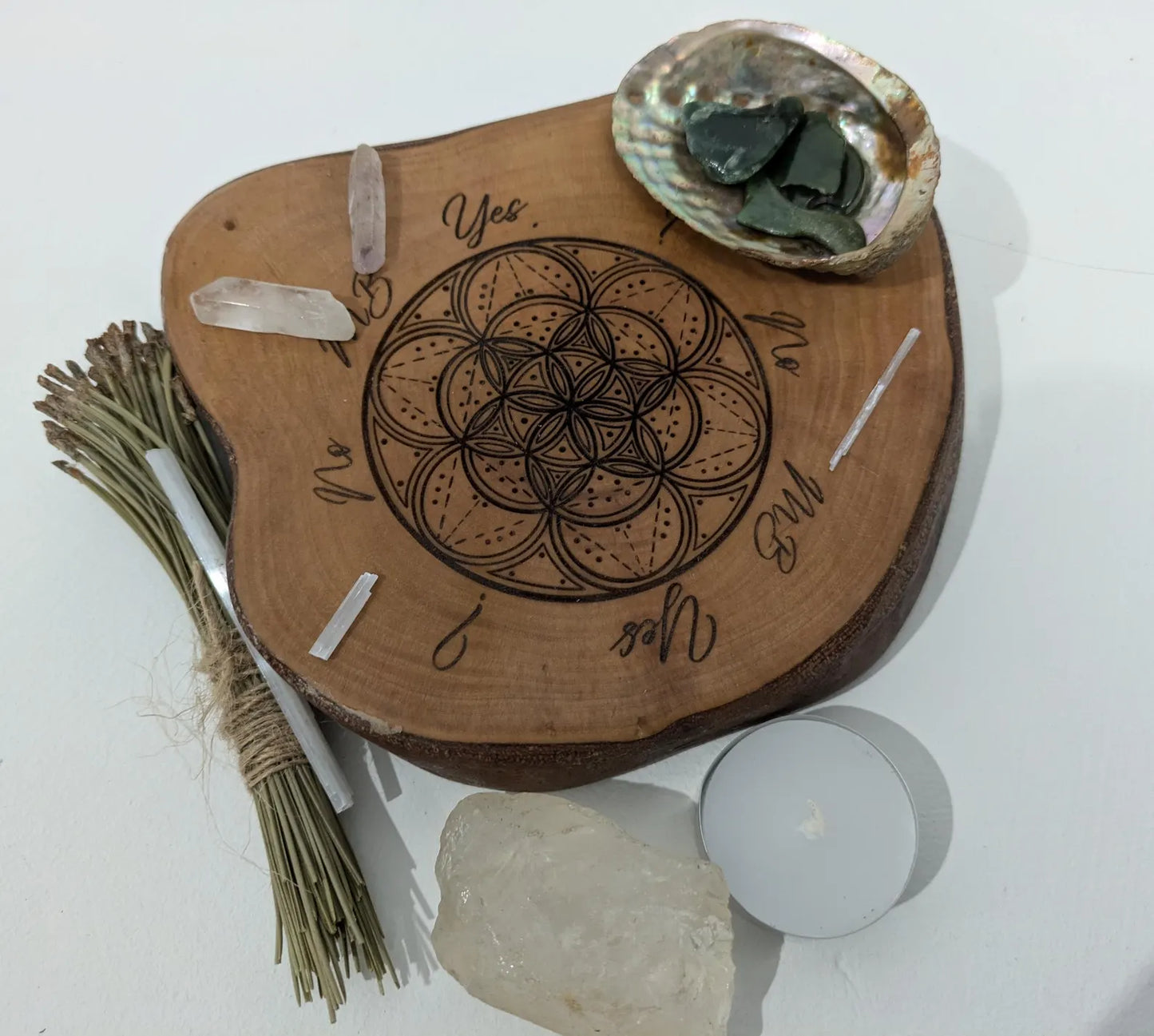 Wooden tree slice dowsing board with geometric laser print design, incense stick holder and loose abalone shell for crystals and herbs.
