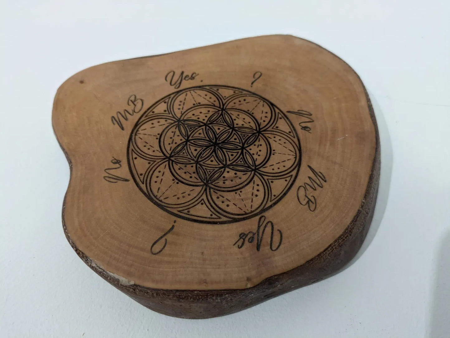 Wooden tree slice dowsing board with geometric laser print design, incense stick holder and loose abalone shell for crystals and herbs.