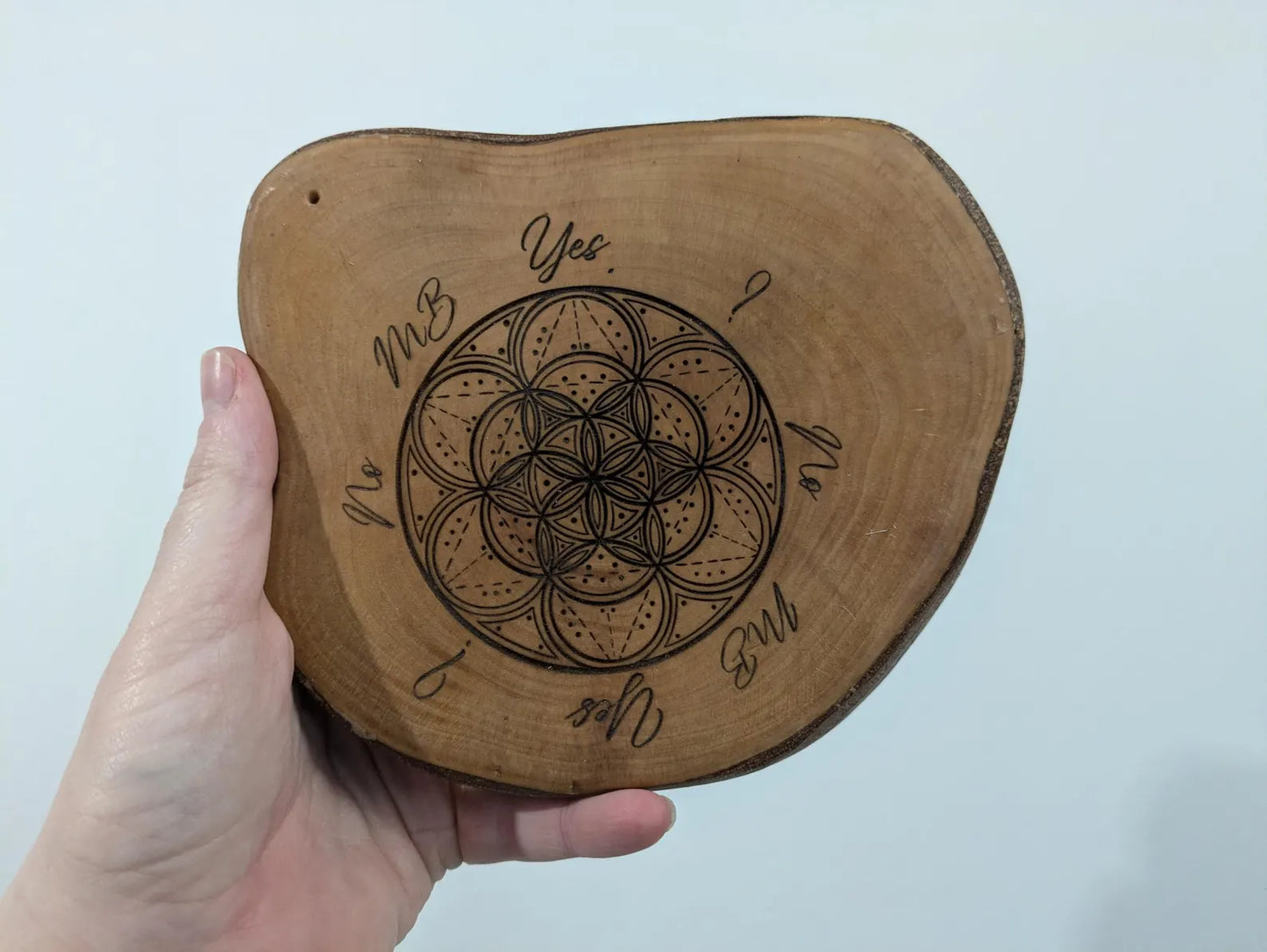Wooden tree slice dowsing board with geometric laser print design, incense stick holder and loose abalone shell for crystals and herbs.