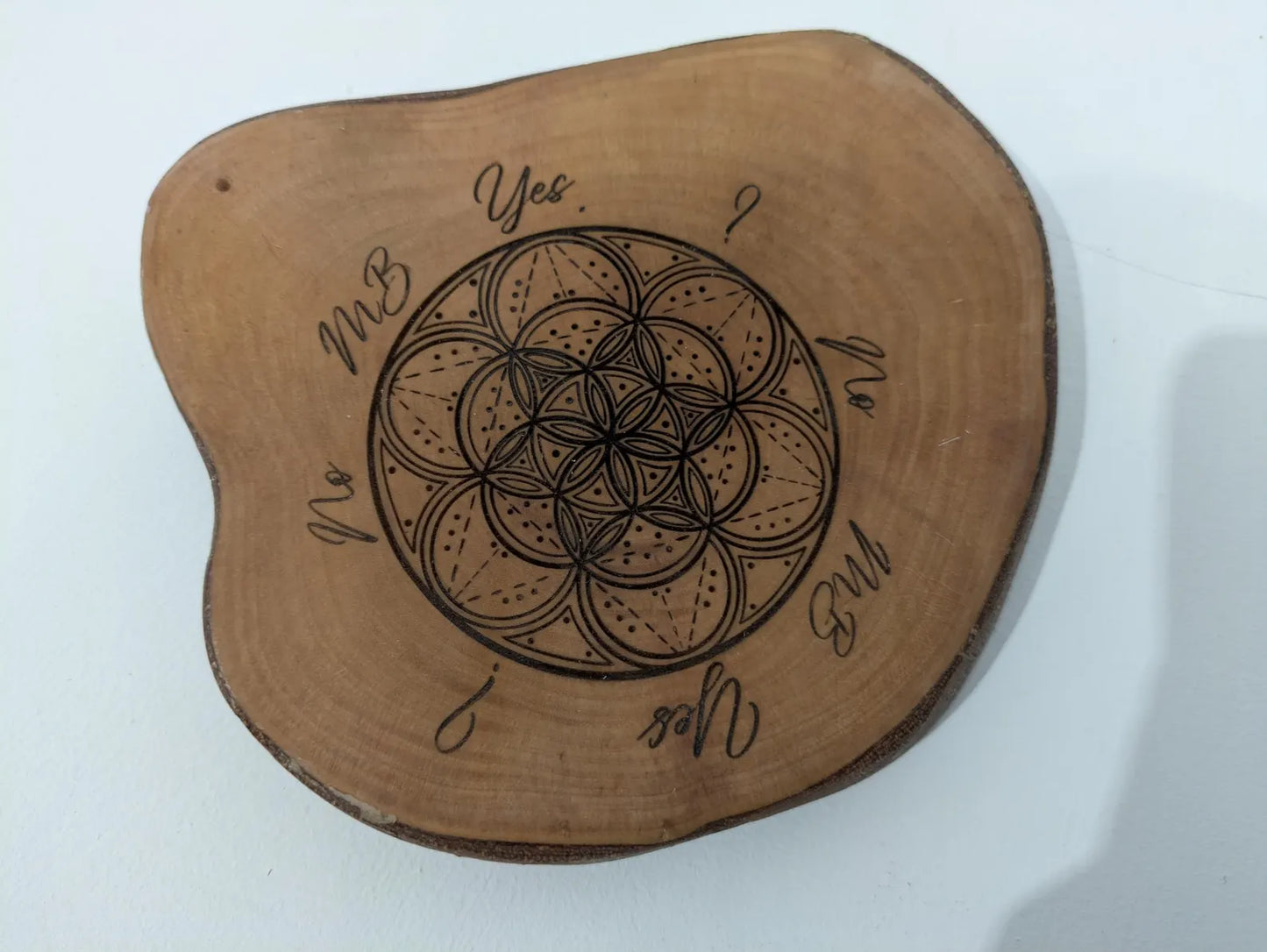 Wooden tree slice dowsing board with geometric laser print design, incense stick holder and loose abalone shell for crystals and herbs.